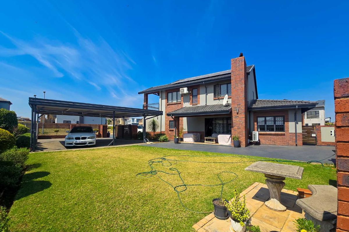 Rear view of a two-story brick house featuring a spacious lawn, paved driveway, and a covered carport area.