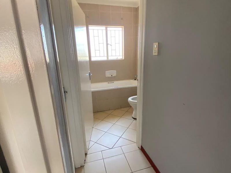A functional bathroom featuring tiled flooring, a built-in bathtub, and a toilet, viewed from the adjacent hallway.