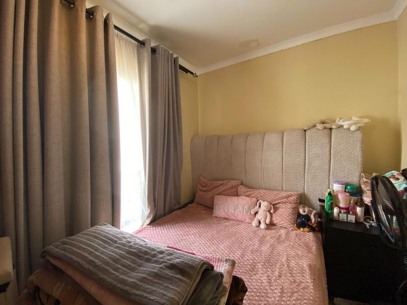 A bedroom featuring a window with curtains and a visible water stain on the ceiling.