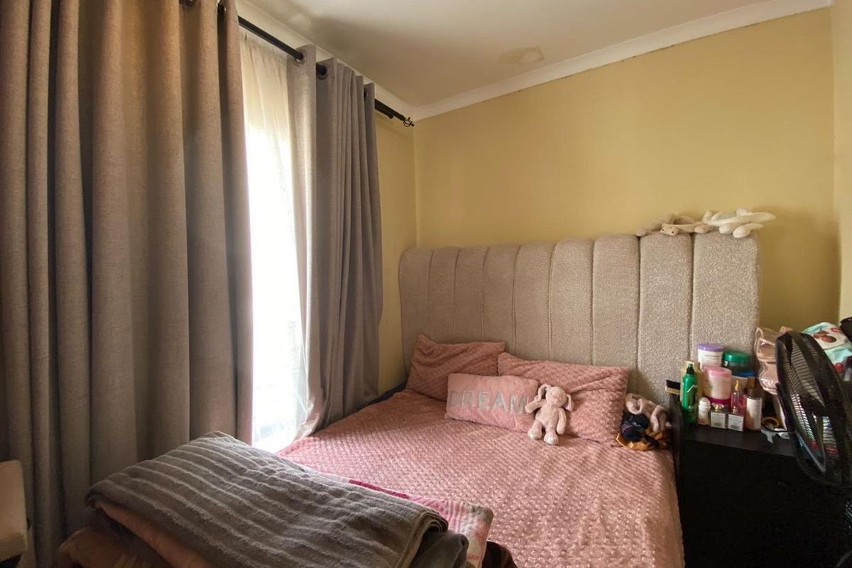 A bedroom featuring a window with curtains and a visible water stain on the ceiling.