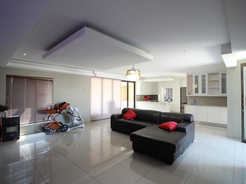 Spacious open-plan living area featuring polished porcelain tiles, a modern kitchen with built-in cabinetry, and a distinctive recessed ceiling design with integrated lighting.