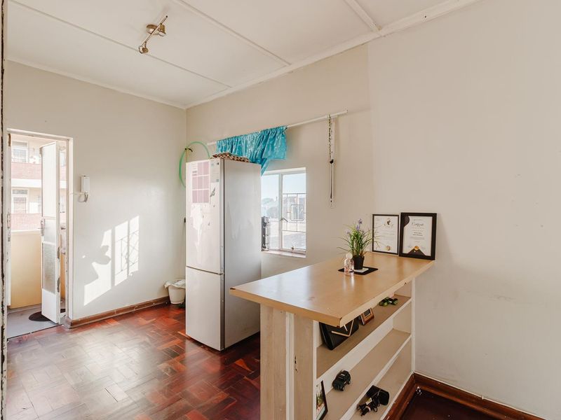 A compact kitchen area featuring parquet flooring, a built-in breakfast bar, and direct access to an exterior balcony.