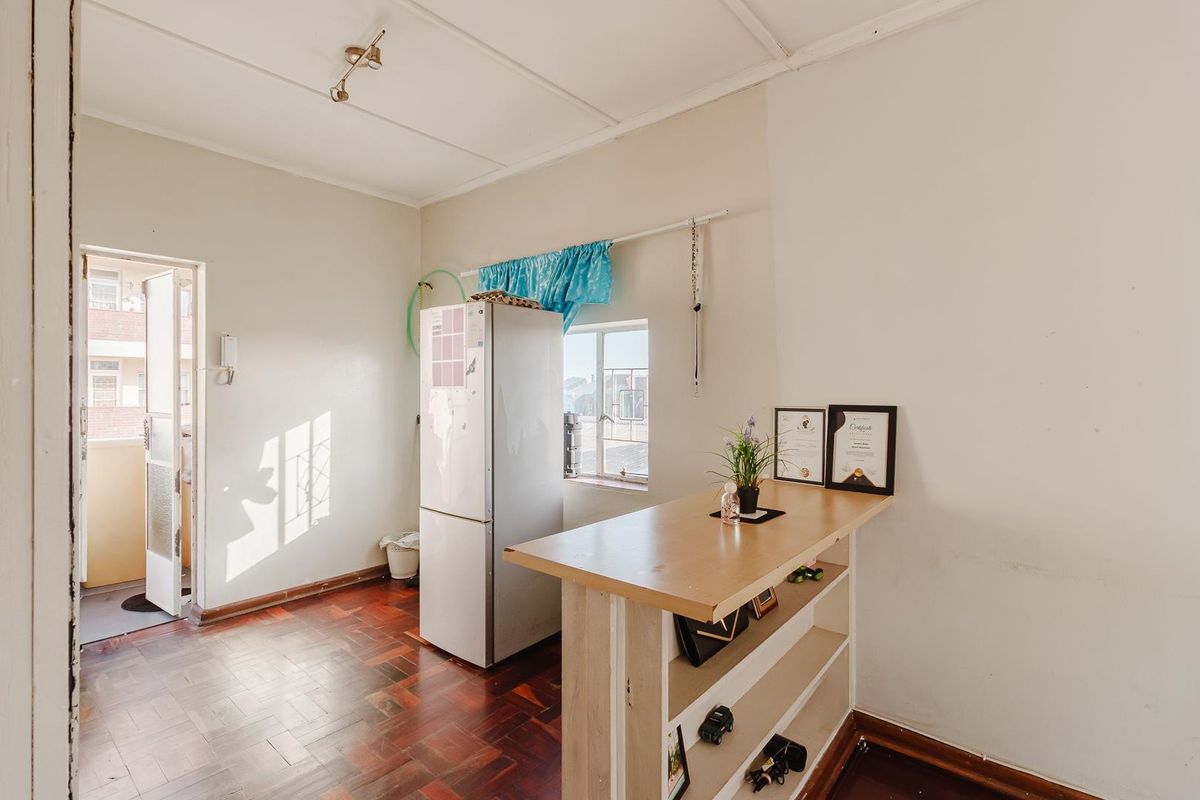 A compact kitchen area featuring parquet flooring, a built-in breakfast bar, and direct access to an exterior balcony.