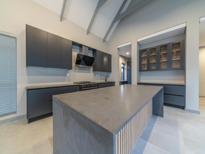Modern kitchen featuring a large central island, dark cabinetry, gas stove, extractor fan, and high vaulted ceilings with exposed rafters.