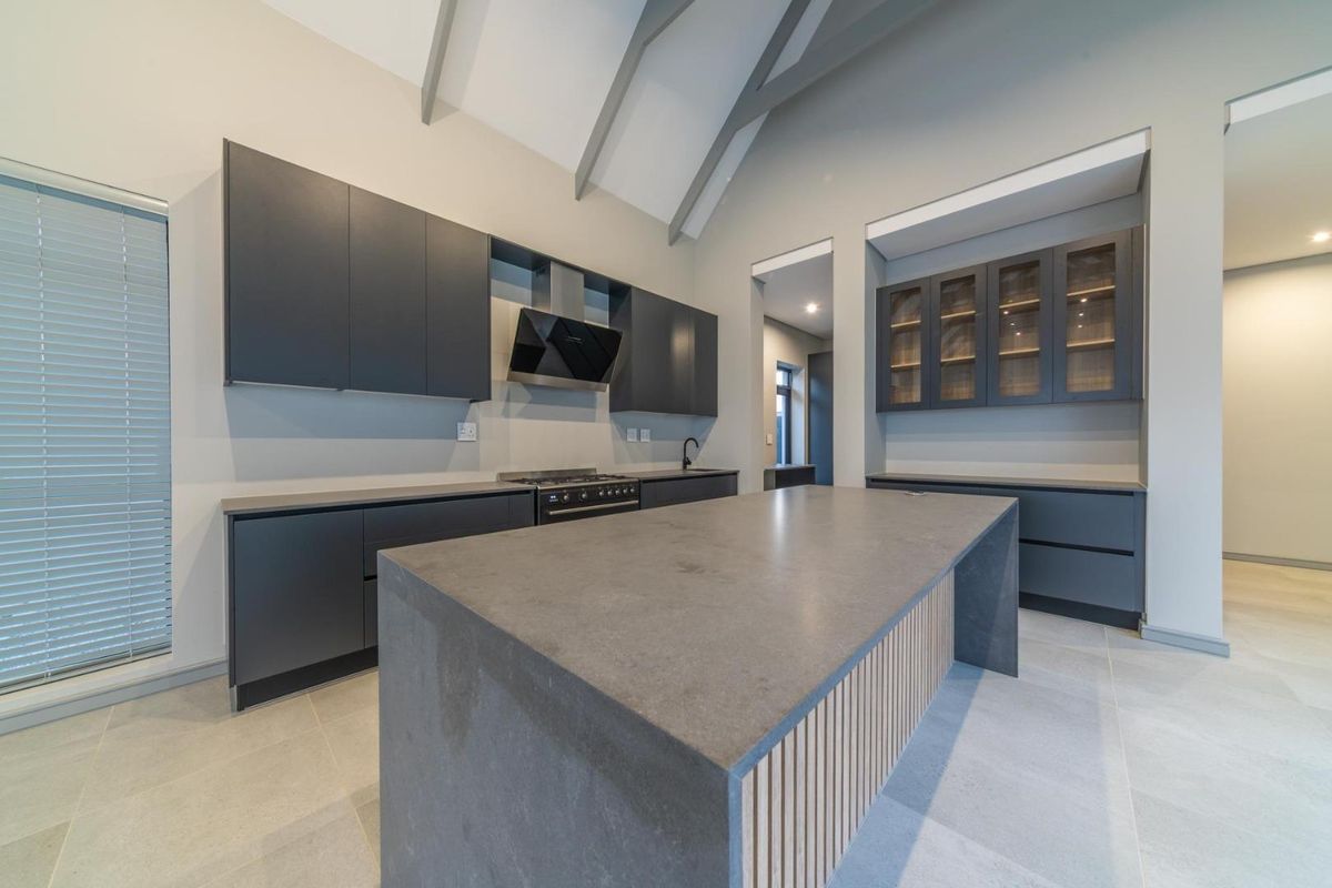 Modern kitchen featuring a large central island, dark cabinetry, gas stove, extractor fan, and high vaulted ceilings with exposed rafters.