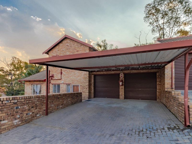 A double garage with an attached carport, featuring face-brick exterior walls and a paved driveway area.