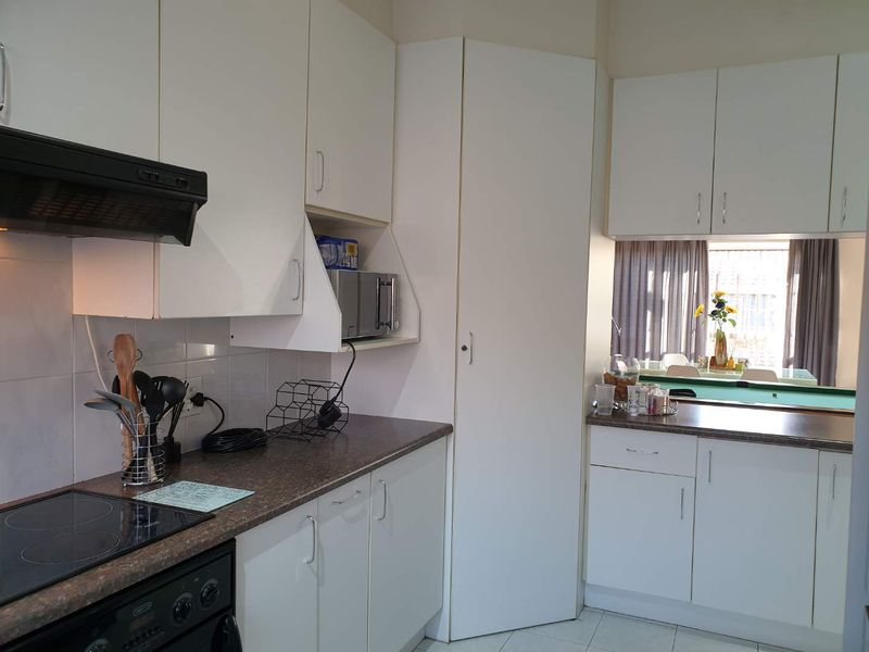 A functional kitchen featuring white built-in cabinetry, dark laminate countertops, an electric hob with extractor fan, and tiled finishes.