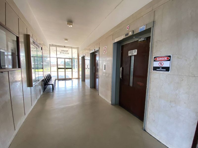 A communal apartment building hallway featuring marble wall cladding, multiple elevator access points, and glass entrance doors leading to the exterior.