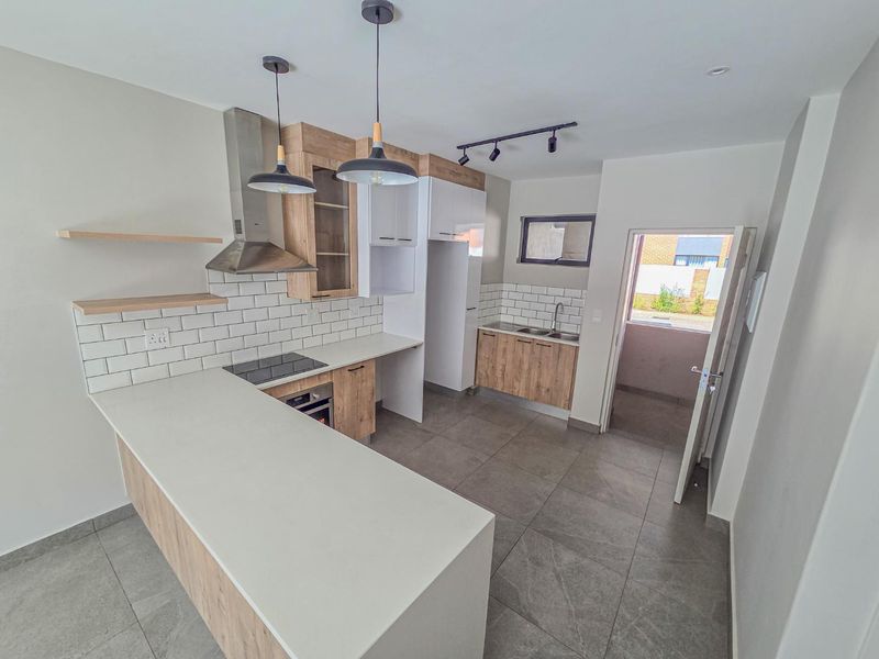 Modern kitchen featuring light wood-grain cabinetry, stone countertops, subway tile backsplash, integrated appliances, and large format floor tiles with direct outdoor access.