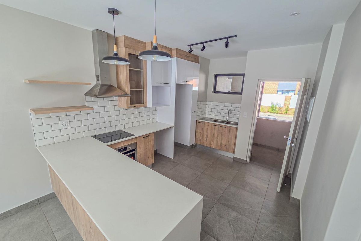 Modern kitchen featuring light wood-grain cabinetry, stone countertops, subway tile backsplash, integrated appliances, and large format floor tiles with direct outdoor access.