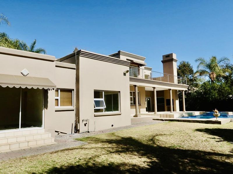 Rear view of the house featuring a swimming pool, covered patio area, upper balcony, and established garden surroundings.