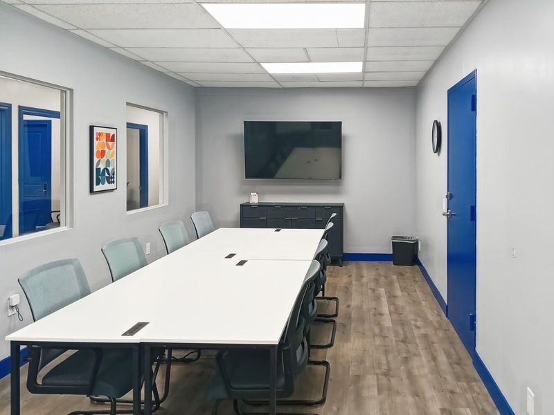A professional office meeting room featuring laminate flooring, drop ceiling with recessed lighting, and interior windows providing a bright, functional workspace.