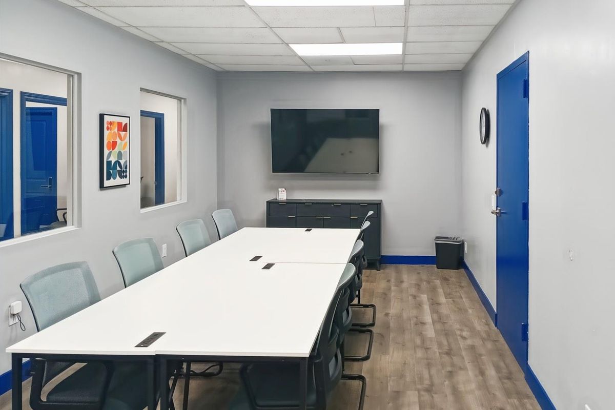 A professional office meeting room featuring laminate flooring, drop ceiling with recessed lighting, and interior windows providing a bright, functional workspace.