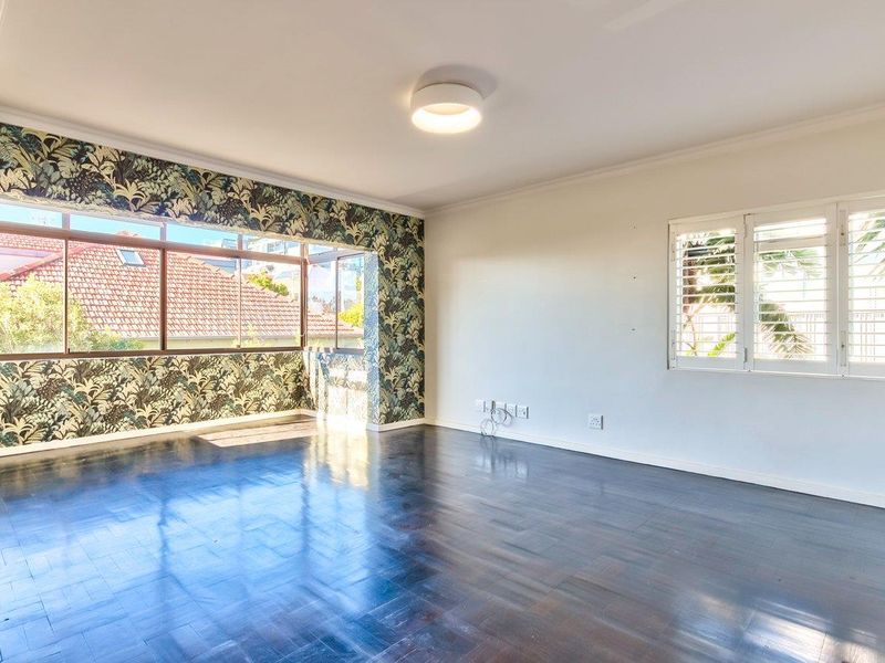 Spacious living room featuring dark parquet flooring, plantation shutters, and a large window with decorative wallpaper accents.
