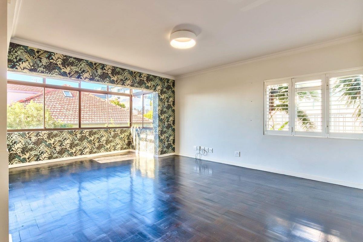 Spacious living room featuring dark parquet flooring, plantation shutters, and a large window with decorative wallpaper accents.