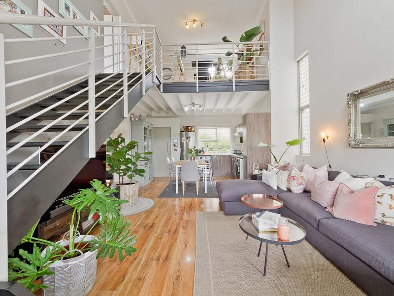 Spacious open-plan living area featuring a mezzanine level, modern metal staircase, hardwood flooring, and a functional kitchen with integrated cabinetry.