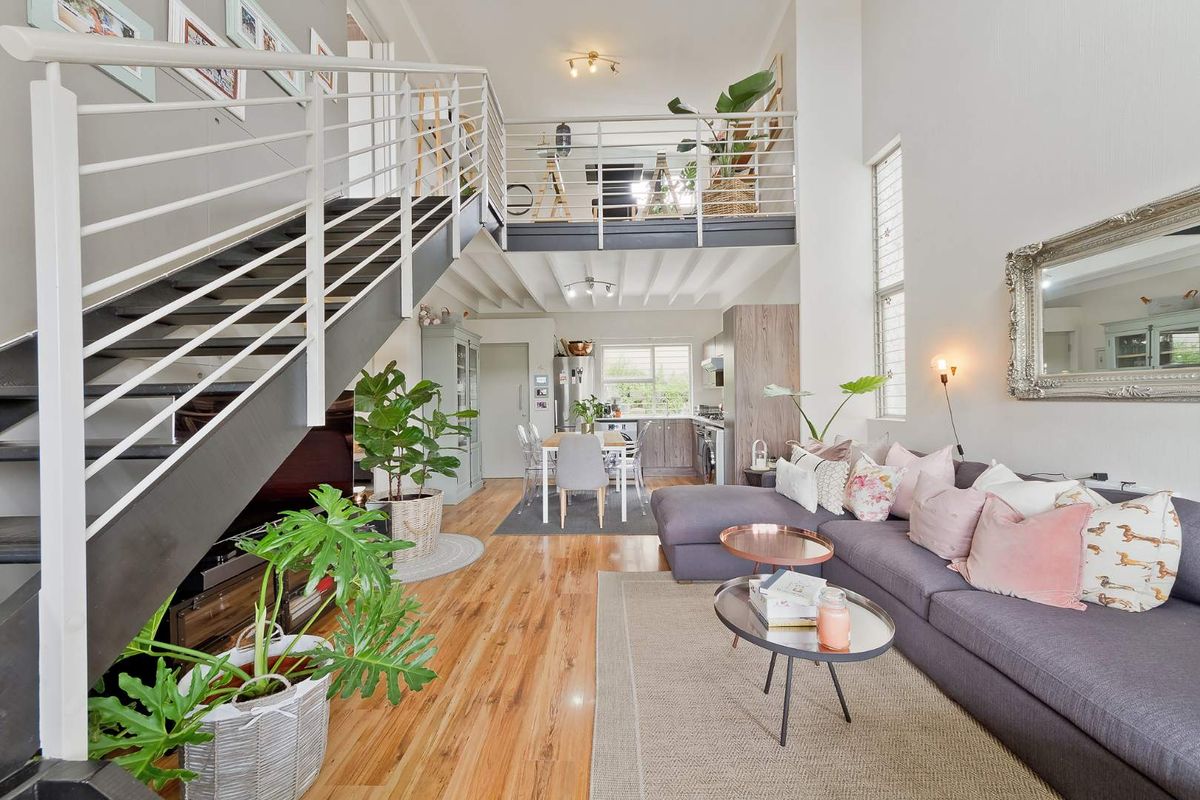 Spacious open-plan living area featuring a mezzanine level, modern metal staircase, hardwood flooring, and a functional kitchen with integrated cabinetry.