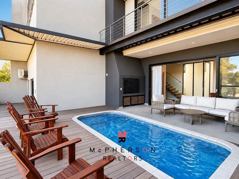 Modern outdoor entertainment area featuring a swimming pool, timber decking, and a covered patio with a built-in fireplace and direct access to the home.