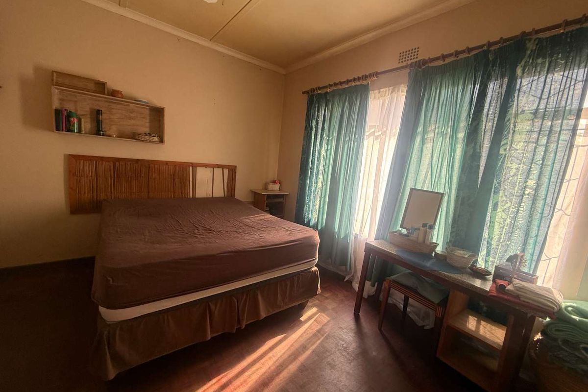 A bedroom featuring parquet flooring, a ceiling fan, and large windows with natural light, offering a functional and comfortable living space.