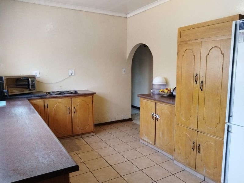 A dated kitchen featuring wooden cabinetry, laminate countertops, and ceramic floor tiles, with an arched doorway leading to an adjacent space.