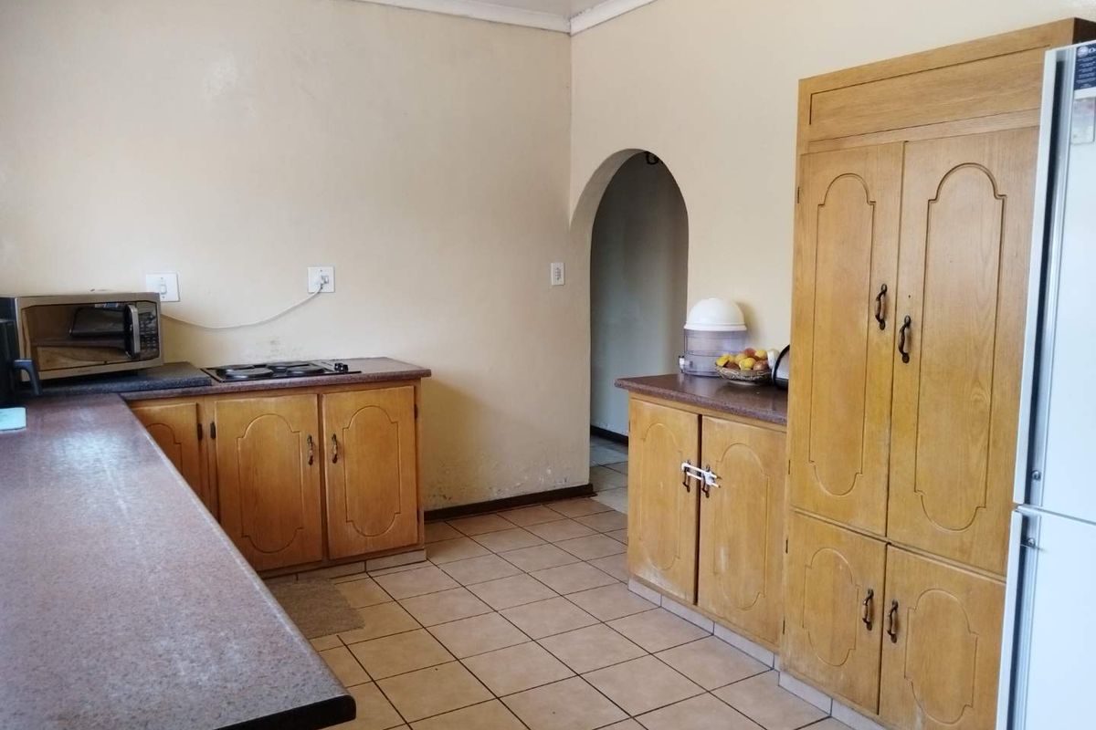 A dated kitchen featuring wooden cabinetry, laminate countertops, and ceramic floor tiles, with an arched doorway leading to an adjacent space.