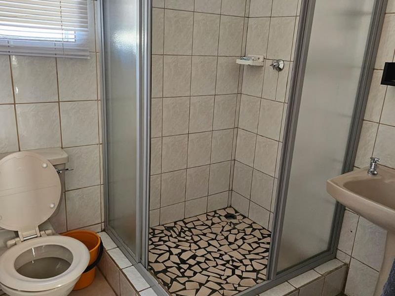 A functional bathroom featuring a shower enclosure, pedestal basin, and toilet with tiled finishes, currently showing signs of wear and dated fixtures.