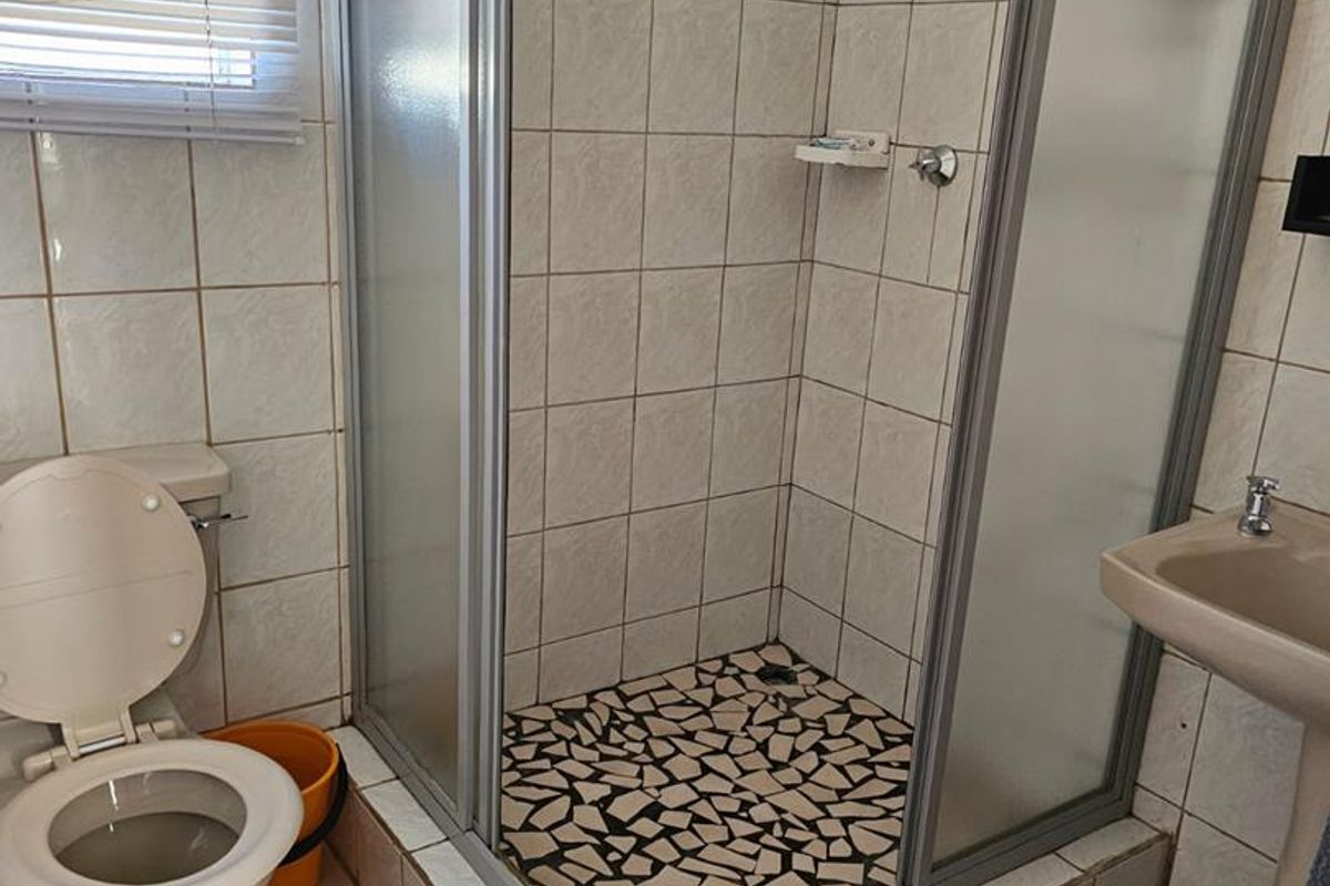 A functional bathroom featuring a shower enclosure, pedestal basin, and toilet with tiled finishes, currently showing signs of wear and dated fixtures.
