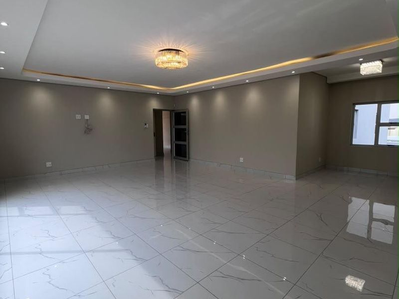 Spacious, modern living area featuring high-gloss marble-look floor tiles, recessed ceiling with ambient cove lighting, and elegant crystal light fixtures.