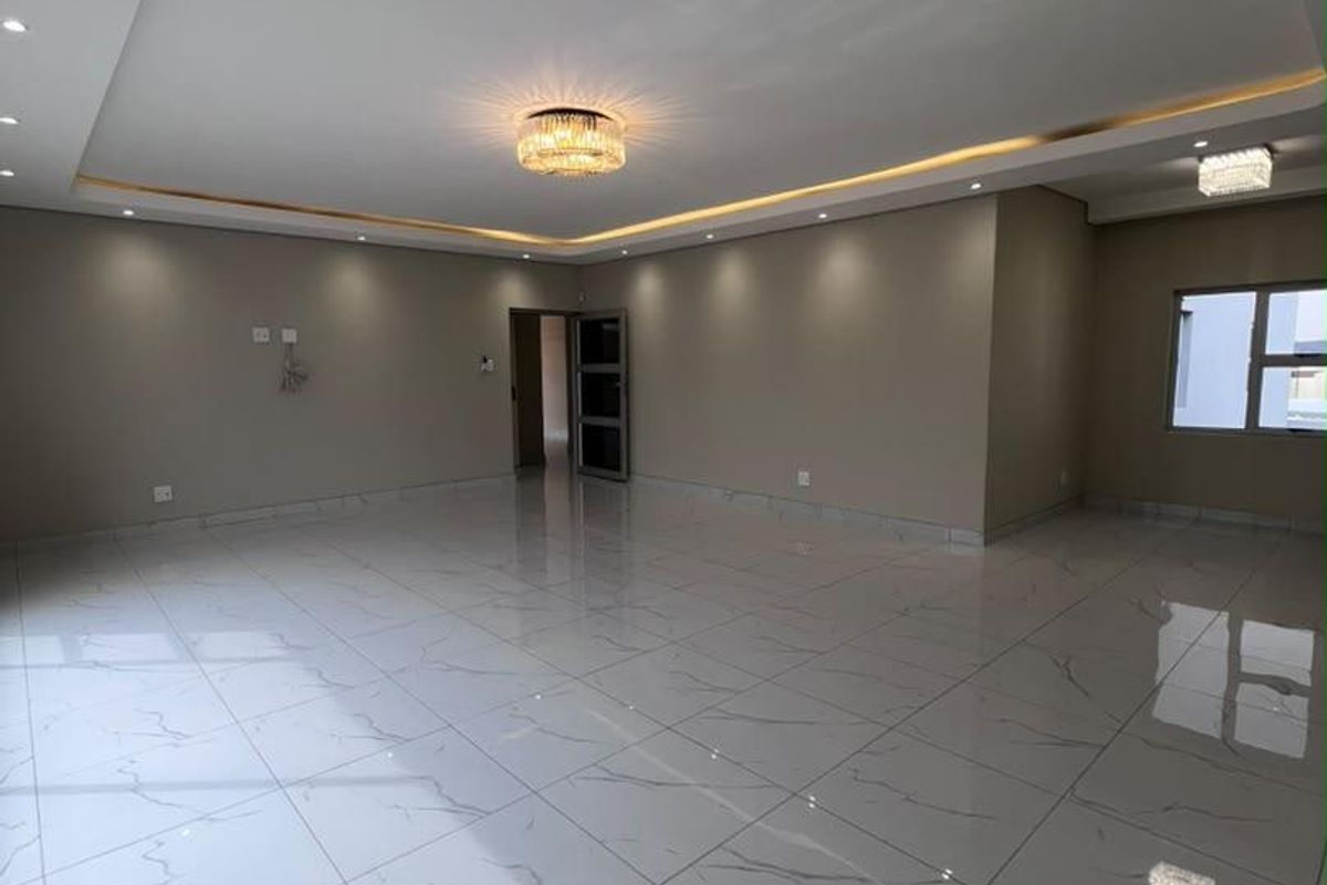 Spacious, modern living area featuring high-gloss marble-look floor tiles, recessed ceiling with ambient cove lighting, and elegant crystal light fixtures.