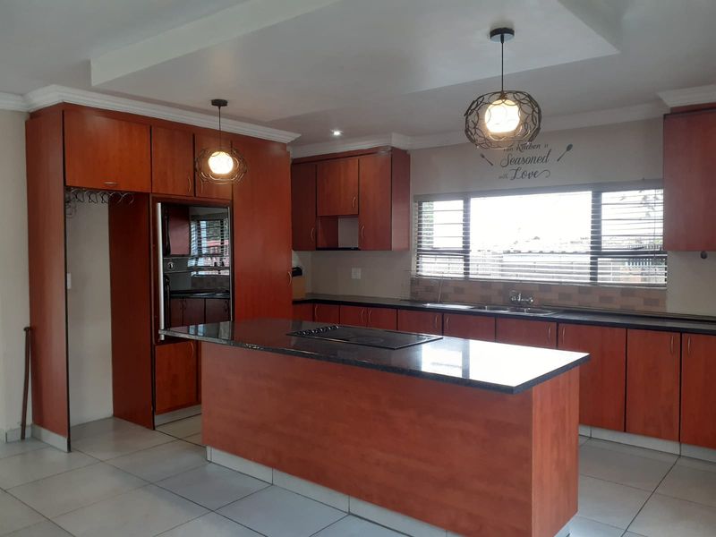 Spacious kitchen featuring warm-toned cabinetry, a central island with a built-in hob, integrated oven, and ample counter space with a double sink.
