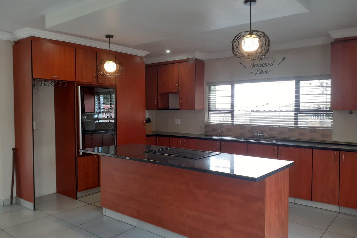 Spacious kitchen featuring warm-toned cabinetry, a central island with a built-in hob, integrated oven, and ample counter space with a double sink.