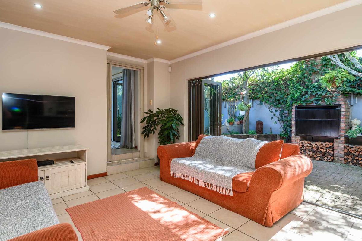 Open-plan living area featuring large bi-fold doors that open onto a paved patio with a built-in brick fireplace and garden access.