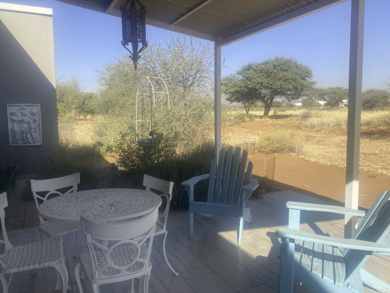 A covered outdoor patio area featuring tiled flooring and a metal roof structure, overlooking a natural bushveld landscape.