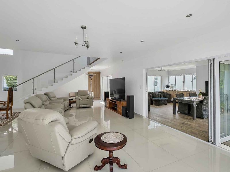 Spacious open-plan living area featuring polished porcelain tiles, a modern staircase with glass balustrades, and seamless indoor-outdoor flow through large bi-fold doors.
