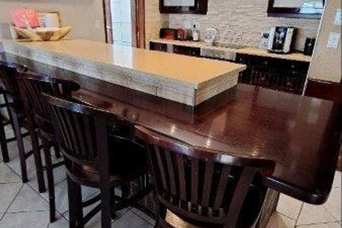 A well-appointed kitchen featuring dark wood cabinetry, a stone-topped breakfast bar, stainless steel extractor fan, and tiled flooring.