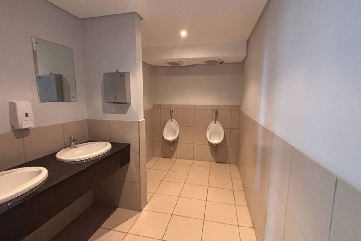 A clean, functional office restroom featuring dual vanity basins, wall-mounted urinals, and neutral tiled finishes throughout.