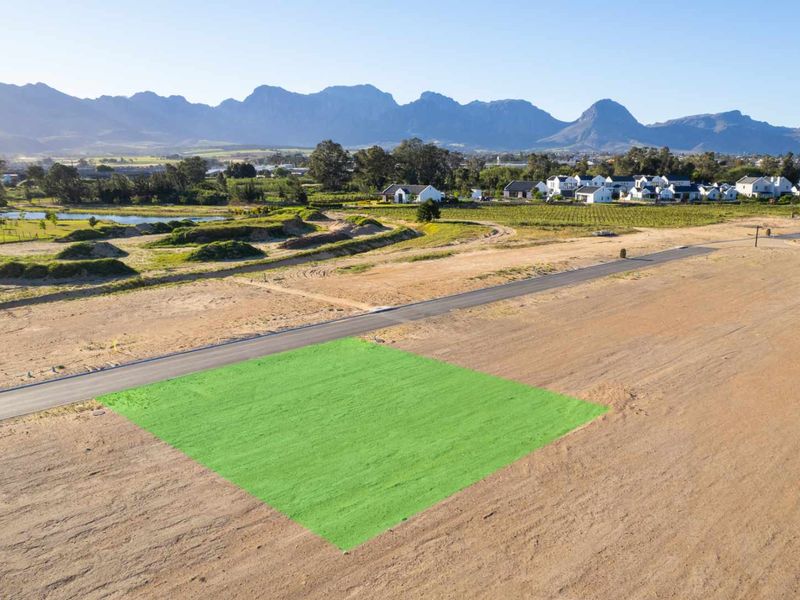 An aerial view of a vacant residential plot with mountain views, situated in a developed estate with paved road access.