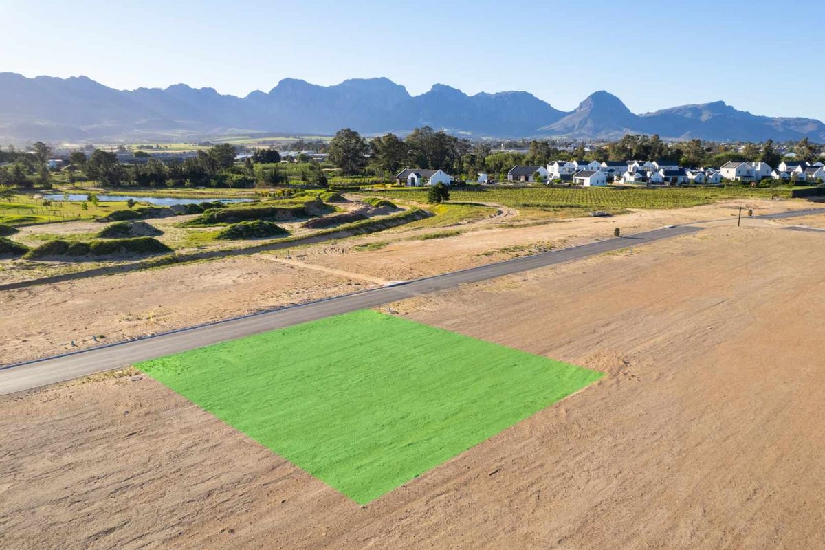 An aerial view of a vacant residential plot with mountain views, situated in a developed estate with paved road access.