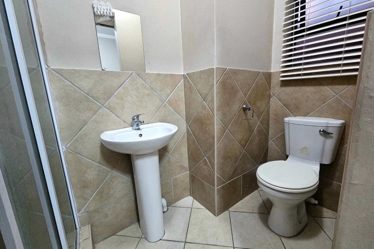 A functional bathroom featuring a pedestal basin, a standard toilet, and a shower enclosure with tiled walls and flooring.