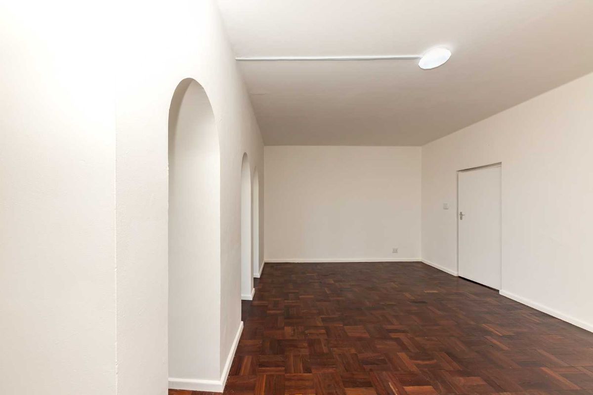 A bright, empty living room featuring classic parquet flooring and distinctive arched wall openings, providing a versatile blank canvas for interior design.
