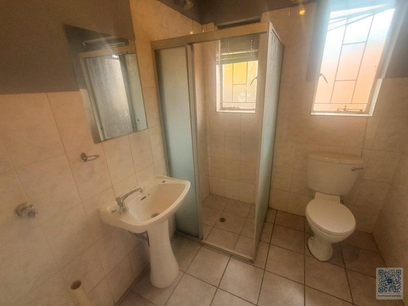 A functional bathroom featuring a pedestal basin, shower enclosure, and toilet with tiled finishes throughout.
