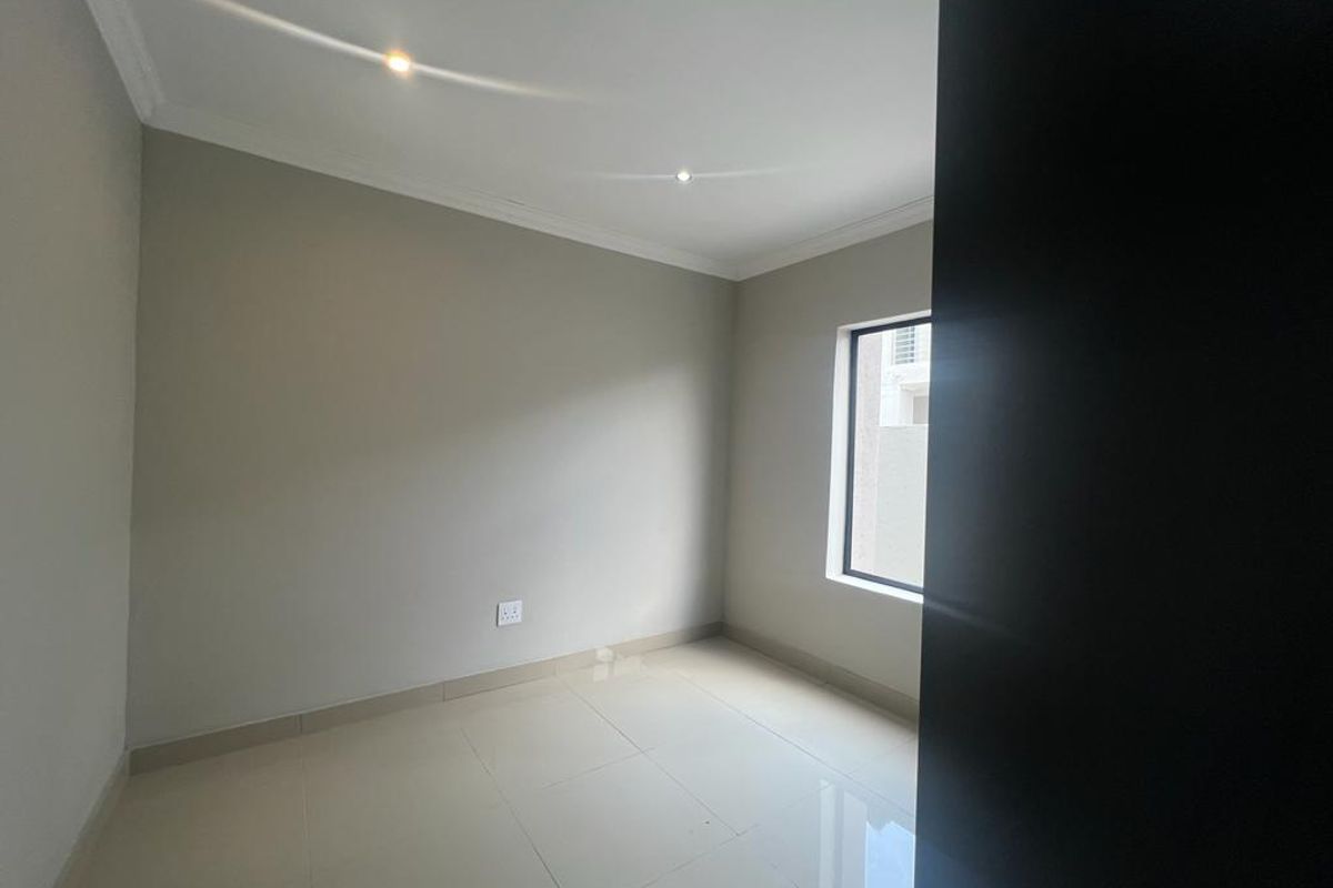 A bright, empty bedroom featuring neutral wall paint, tiled flooring, recessed ceiling lighting, and a window providing natural light.