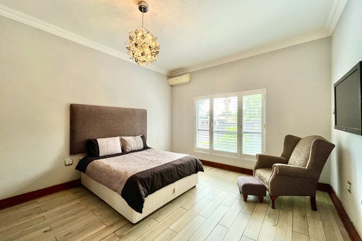 A well-maintained bedroom featuring tiled flooring, crown molding, plantation shutters, and a wall-mounted air conditioning unit.