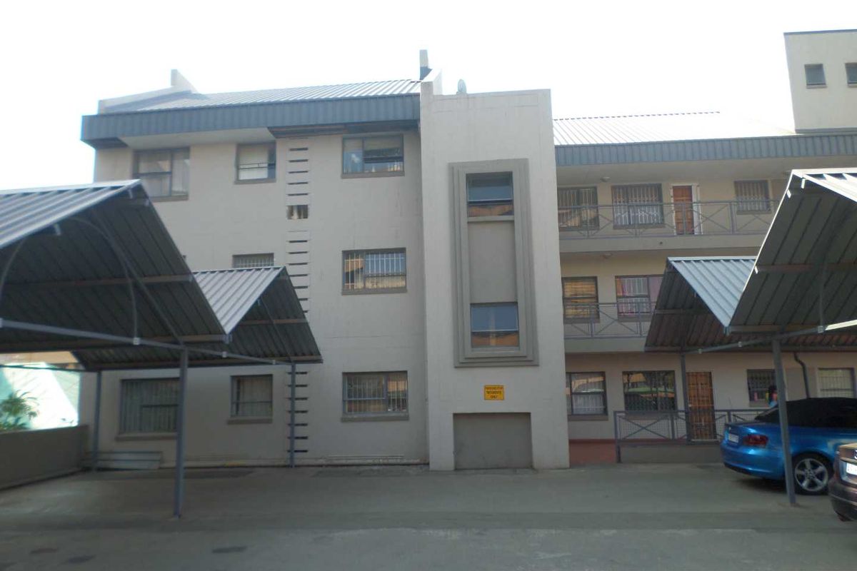 Exterior view of a multi-story apartment building featuring covered parking carports and balcony access with security bars on windows.