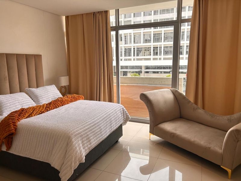 A well-lit bedroom featuring large floor-to-ceiling windows with access to a balcony, complemented by modern tiled flooring.