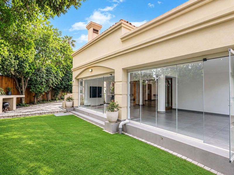 A well-maintained rear exterior featuring a manicured lawn, paved walkway, built-in outdoor counter, and modern stacking glass doors leading into the home.