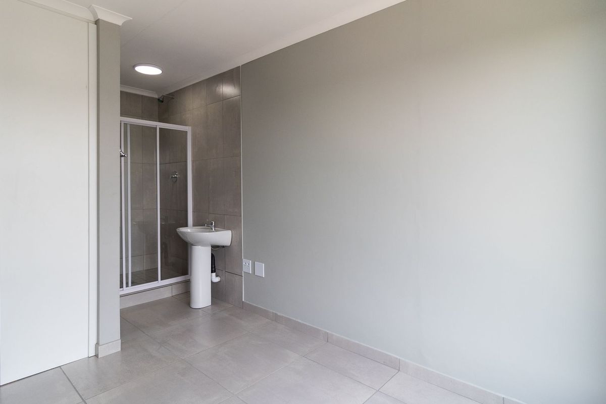 A clean, modern bathroom featuring a pedestal basin, a glass-enclosed shower, and neutral floor-to-ceiling tiling, presenting a well-maintained and functional space.