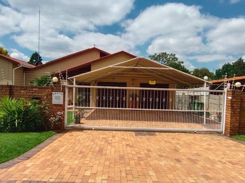 Front view of the property featuring a paved driveway, secure sliding gate, double garage with a carport, and brick boundary wall with electric fencing.