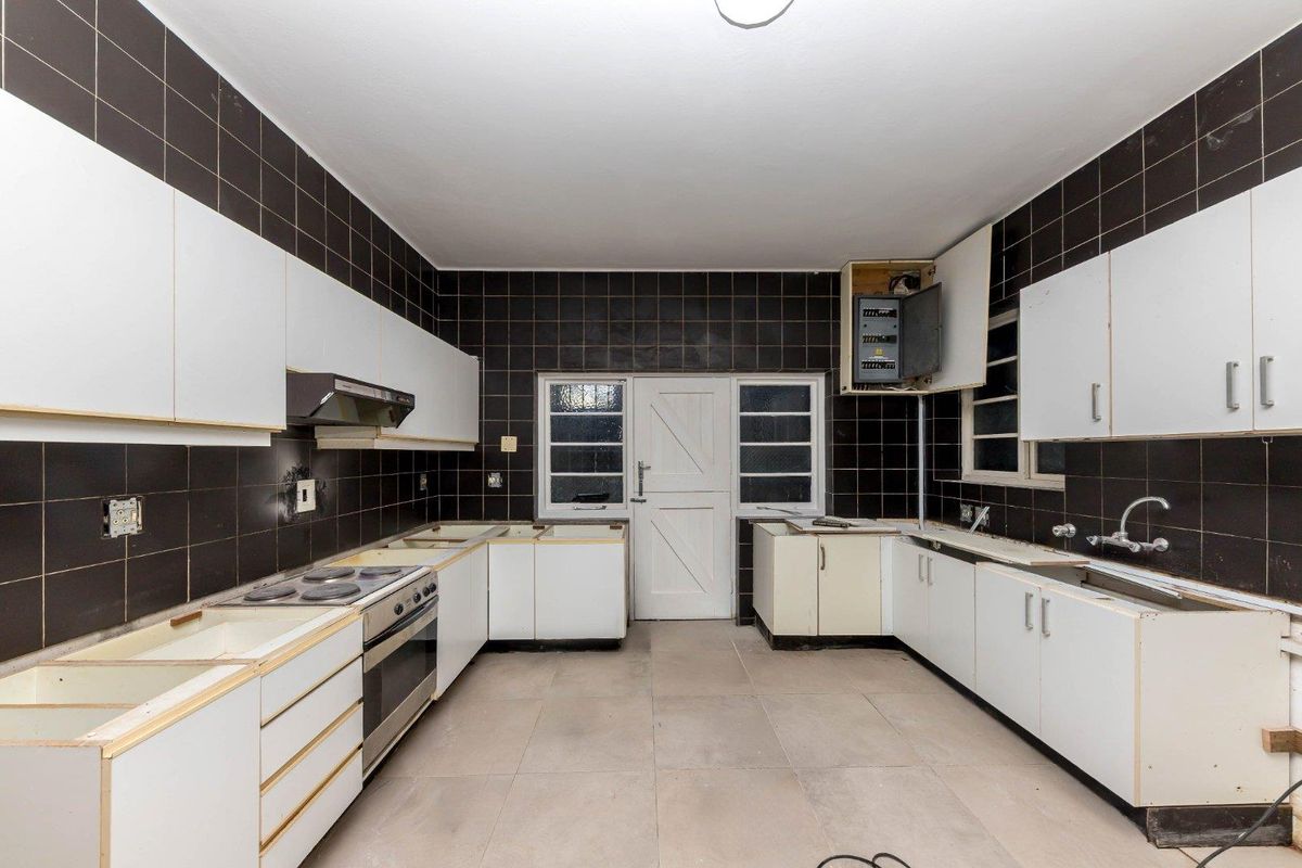 A dated kitchen featuring black wall tiles, white cabinetry, and a built-in oven and hob, currently requiring significant renovation and countertop installation.