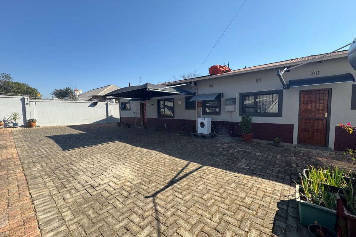 Rear exterior view of the property featuring a paved courtyard, boundary wall, and security features on windows and doors.